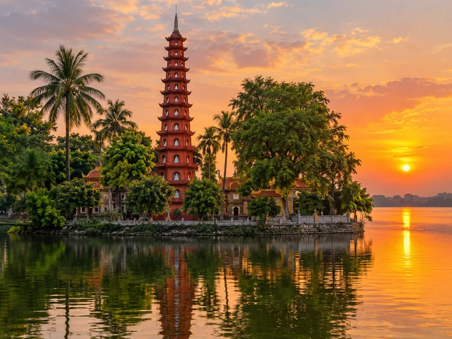 Der hohe Stupa aus rotem Backstein der Tran-Quoc-Pagode spiegelt sich bei Sonnenuntergang im Westsee